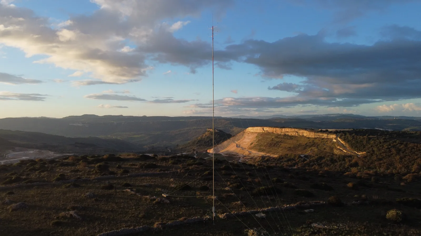 Crinale collinare al tramonto con una torre anemometrica che si staglia contro il cielo