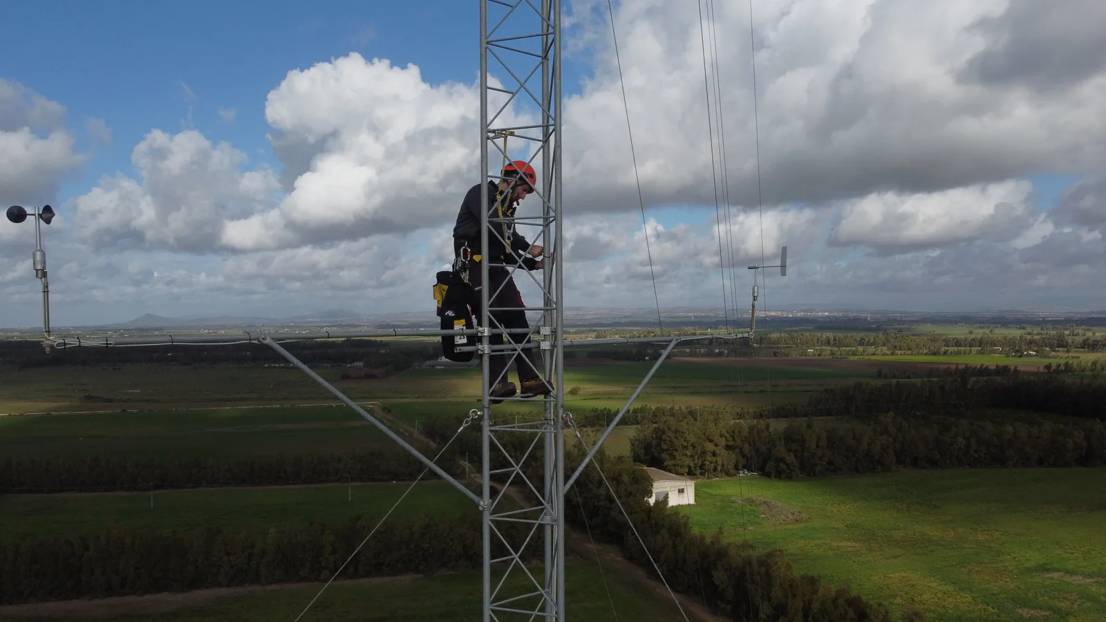 Un tecnico sale in sicurezza lungo un traliccio anemometrico sopra i campi coltivati