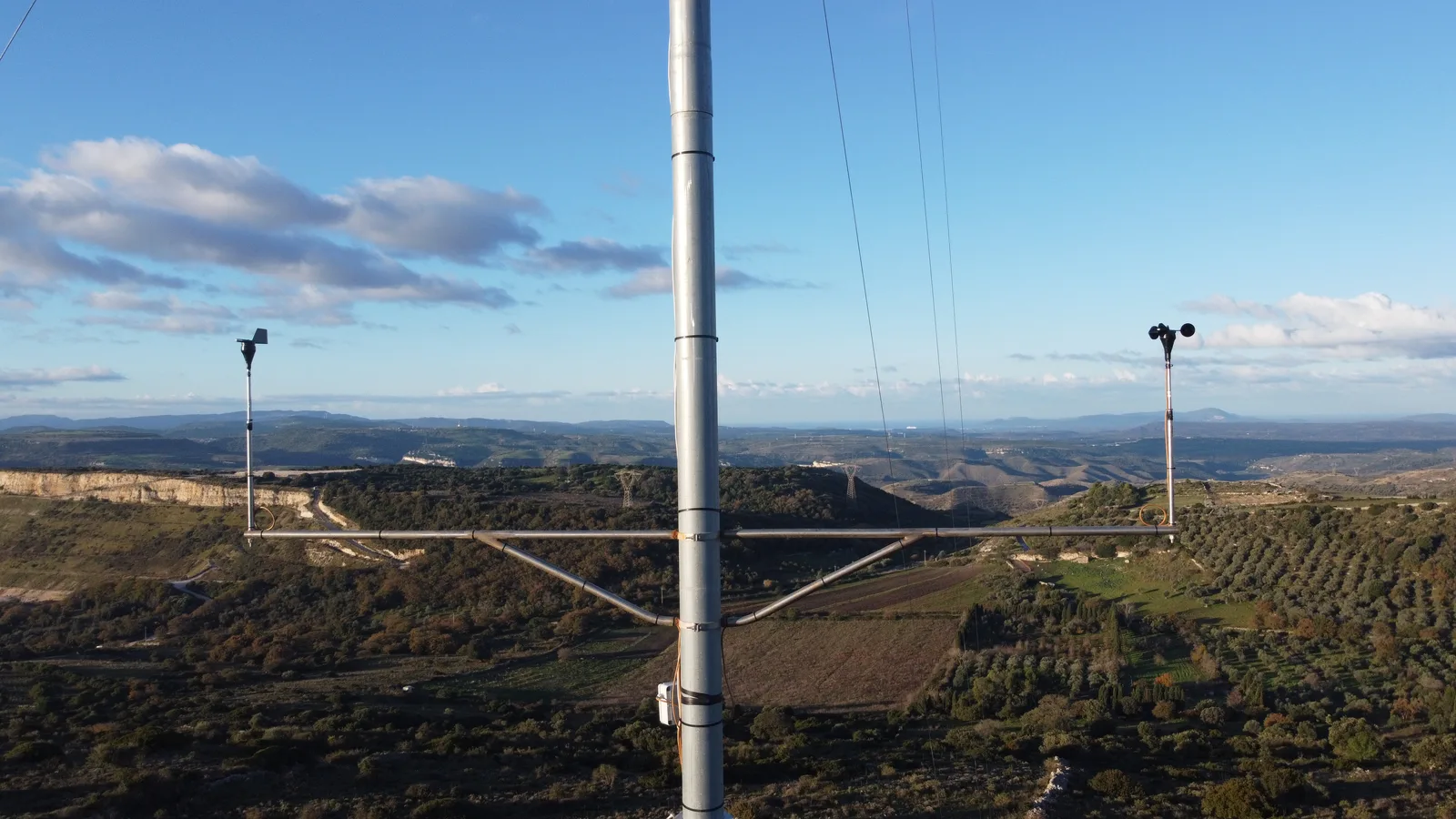 Bracci portasensori con anemometri montati in quota su una torre a palo, valle sullo sfondo